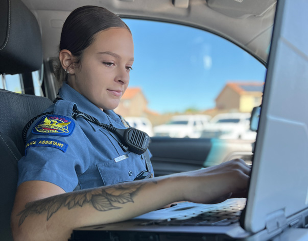 A female police assistant with the PHX PD using a laptop in a car.