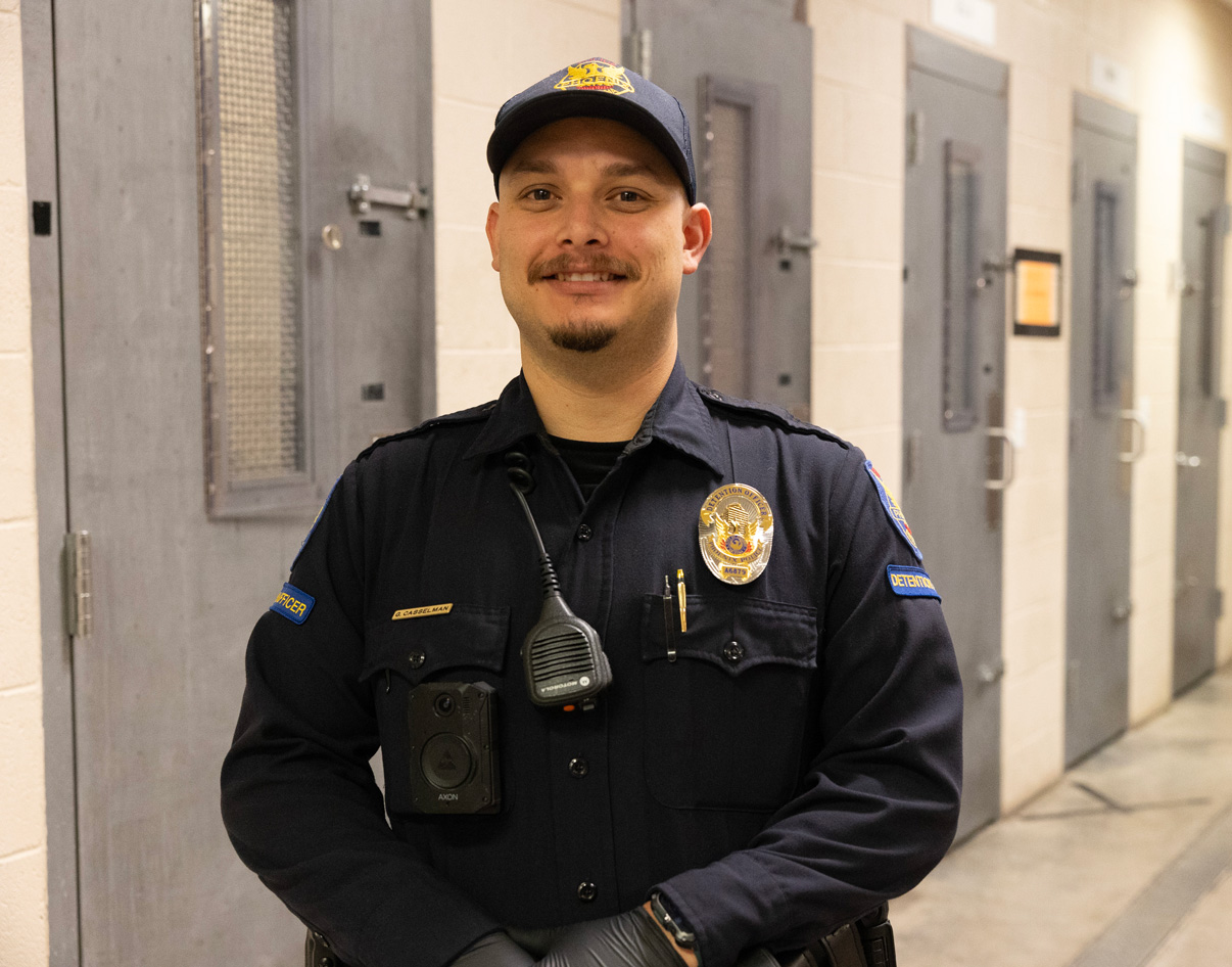 A PHX PD detention officer standing in a hallway of cell doors.