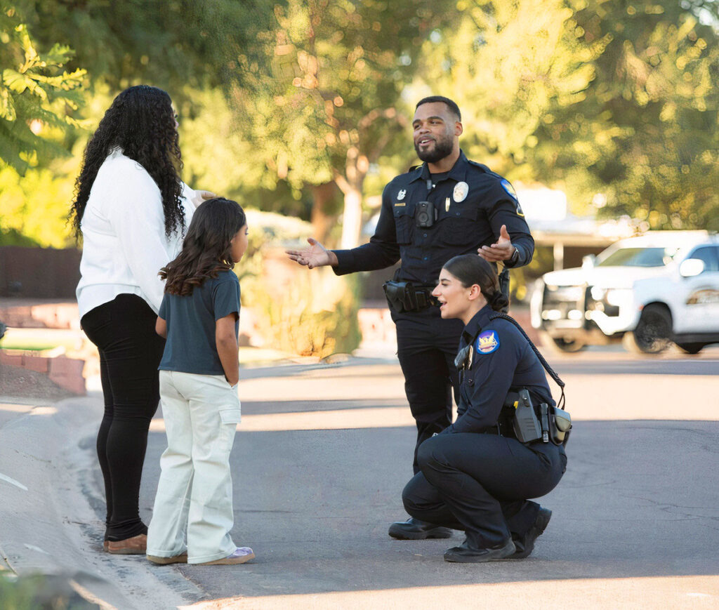 Two police officers from #JOINPHXPD talking to a woman and a child on the street.